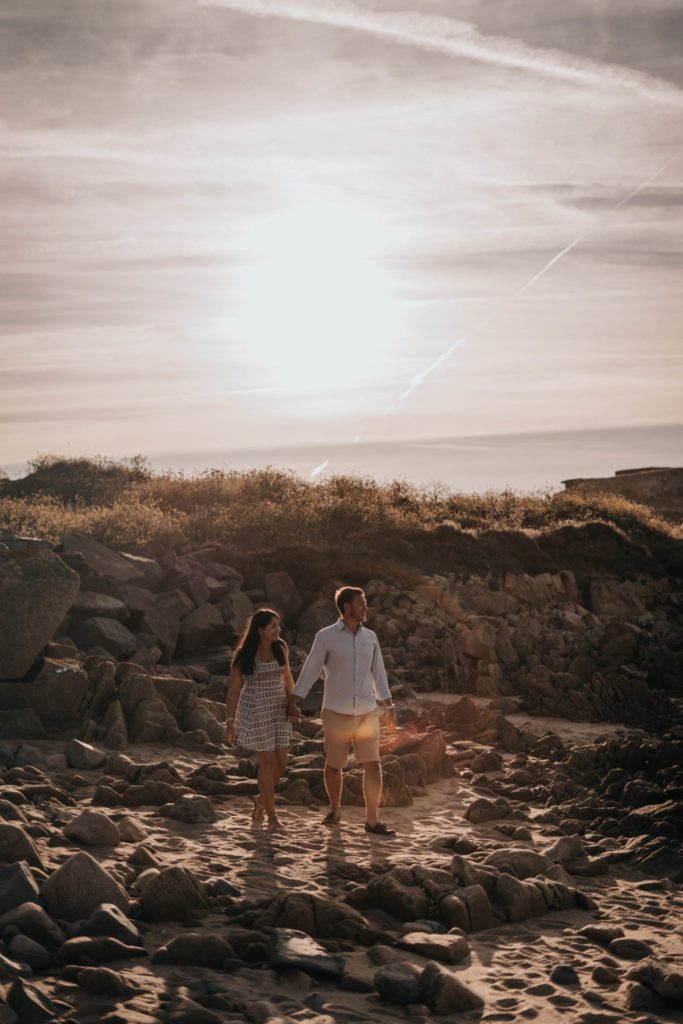 couple holding hands and walking towards the sea